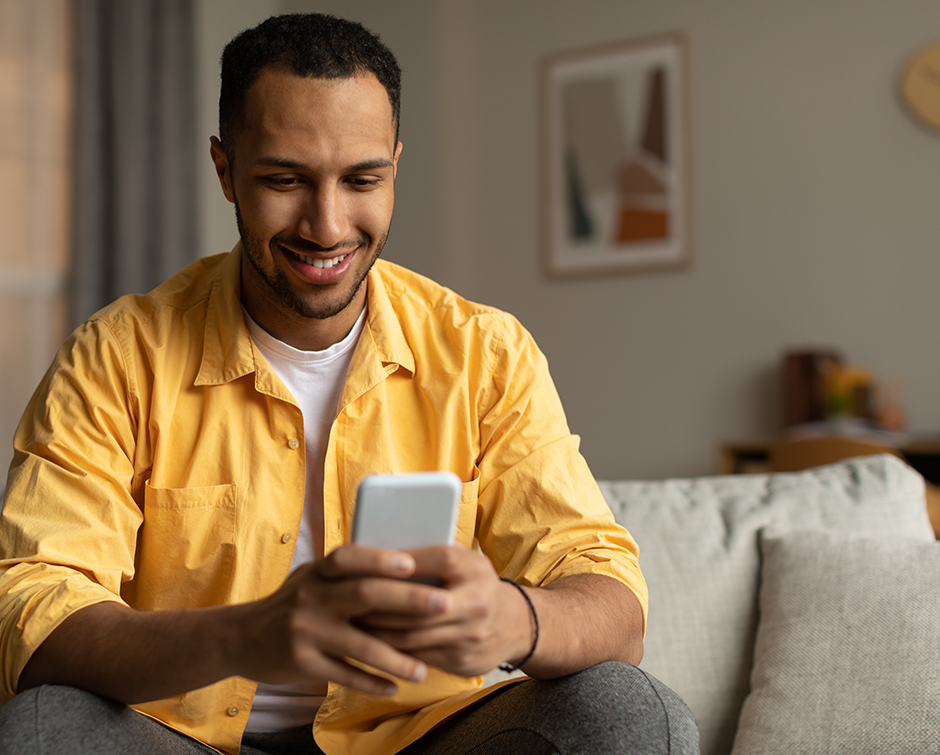 joyful-young-black-guy-using-smartphone-video-chatting-with-friend-browsing-social-media-sitting-sofa-home